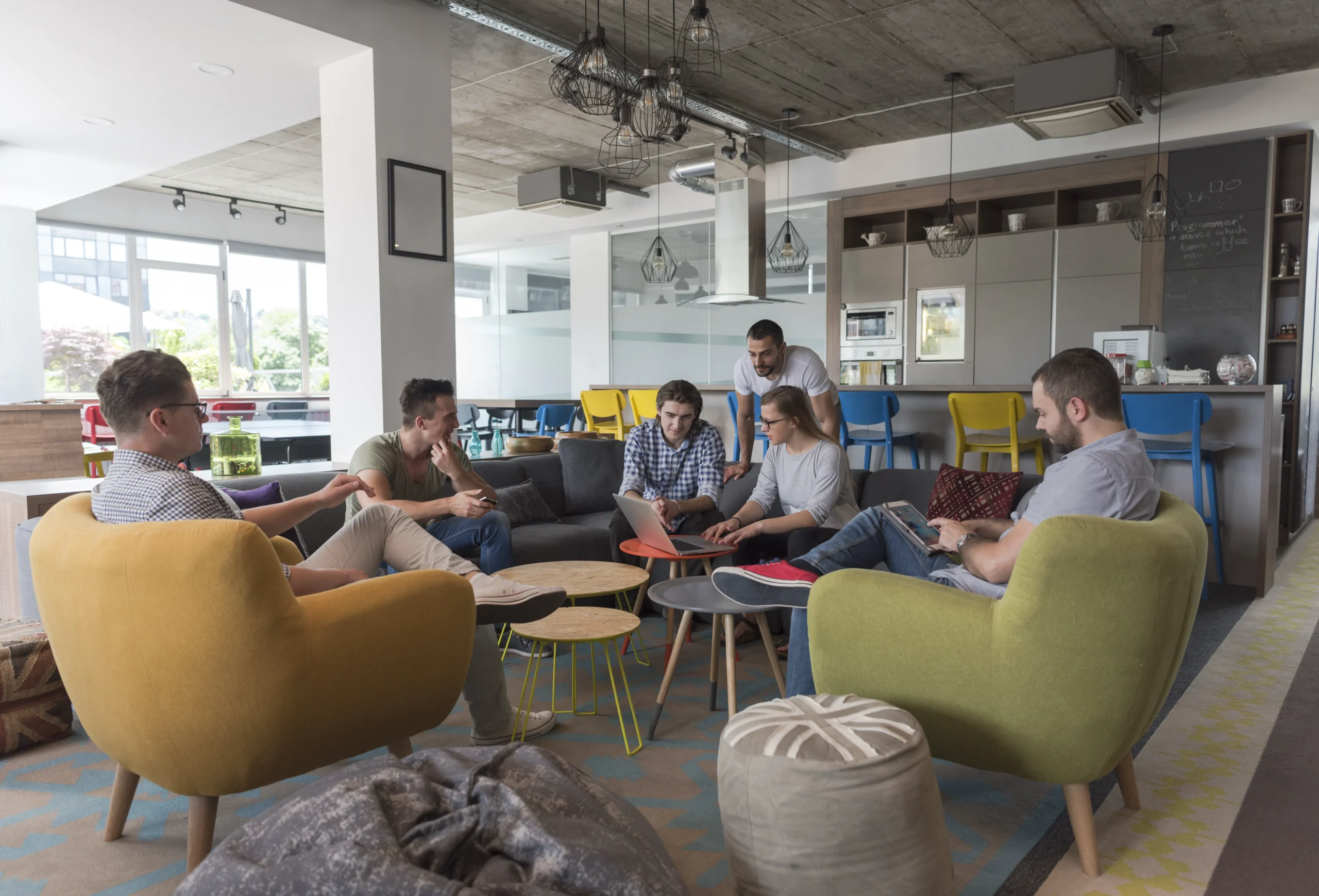 group of coworkers seated in a bright open plan office lounge talking and using laptops